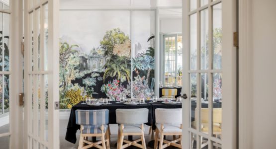 An open door to a dining room set with coloured chairs, a black table cloth, and colourful art